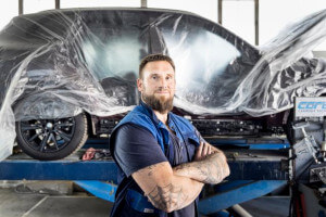Fachmann in einer Karosseriefachwerkstatt vor einem schwarzen Auto